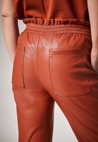 Läderbyxor i en bränd orange färg med elastisk midja, som har två bakfickor med sömdetaljer. Slät textur.