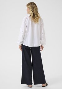 White cotton blouse with lace embroidery on long sleeves, paired with dark wide-leg pants. The outfit features a relaxed fit and minimal details.