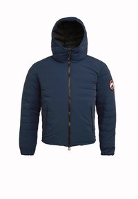 Marineblå pufferjakke med hætte, med lynlås lukning og to lynlåslommer på siden. Inkluderer et rundt logo-patch på venstre ærme.