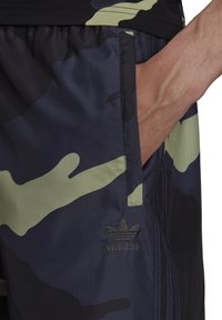 Shorts mimetici blu e verdi, realizzati in tessuto leggero, con una tasca laterale e logo adidas ricamato vicino all'orlo.