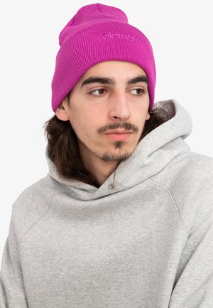 Berretto a maglia rosa con texture a coste e logo ricamato, indossato con una felpa in pile grigia chiara dotata di cappuccio e tasca.