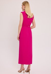 Fuksjowa, bezrękawna sukienka maxi z dopasowanym pasem i elastycznymi detalami. Gładki materiał; zawiera subtelny złoty guzik z tyłu.