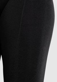 Zwarte leggings met een gestructureerde afwerking, voorzien van een subtiel logopatroon aan de zijkant en een slim-fit ontwerp voor flexibiliteit en comfort.