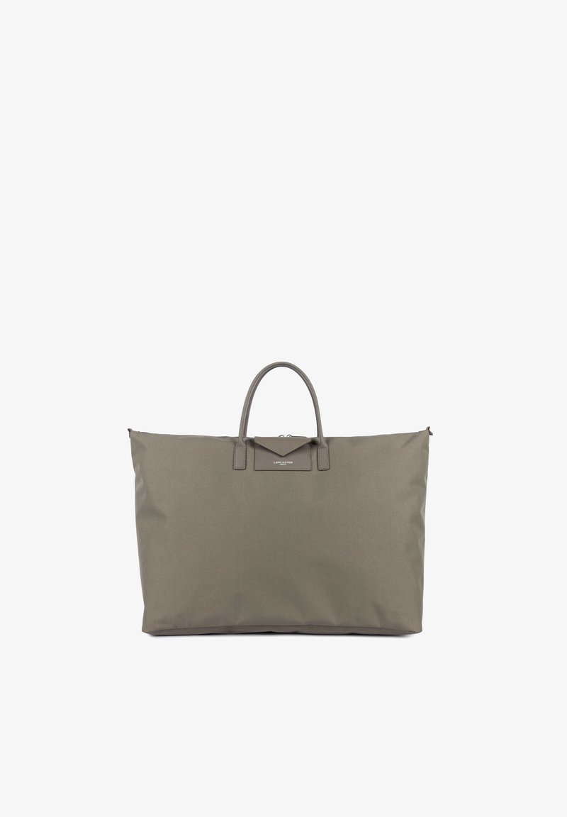 Grand sac cabas taupe avec deux poignées courtes et petit rabat avant avec étiquette de marque sur fond blanc uni.