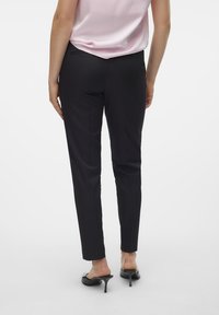Fekete, slim fit szabású nadrág sima anyagból, közepes derékkal és diszkrét hátsó zsebekkel, párosítva nyitott orrú fekete magassarkúval.