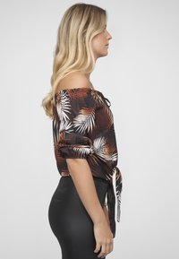 Blouse à épaules dénudées en tissu foncé avec un motif de feuilles tropicales en blanc et orange. Manches courtes froncées et un lien à la taille.