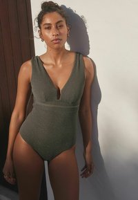 Olive green ribbed one-piece swimsuit with a deep V-neck and wide shoulder straps, featuring a fitted silhouette and subtle shimmer.