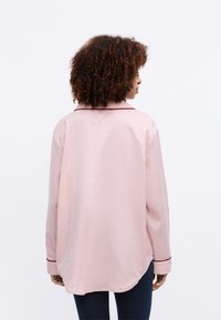 Långärmad rosa skjorta med en slät textur, med en kontrasterande mörk krage och manschetter, samt en rundad nederkant bak.