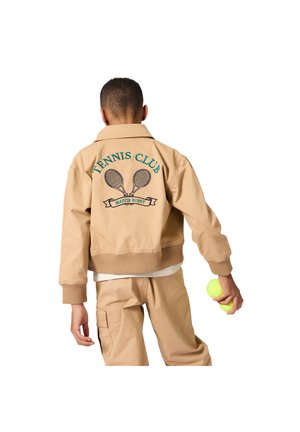 Bēša bombere jaka ar ribotu aproci un apakšu. Aizmugurē zaļa izšuvuma uzraksts “TENNIS CLUB” un krustotas tenisa raketes. Persona tur rokā tenisa bumbiņu.