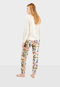 Lichtgekleurde langemouwen top gecombineerd met gestreepte sweatpants met bloemen- en bladdesigns en tekstaccenten; elastische manchetten bij de broekspijpen.