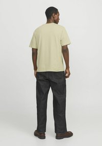 Helles grünes T-Shirt mit kurzen Ärmeln, kombiniert mit dunklen Jeans. Das T-Shirt hat einen klassischen Schnitt; die Hose hat eine lockere Passform mit sichtbaren Nähten.