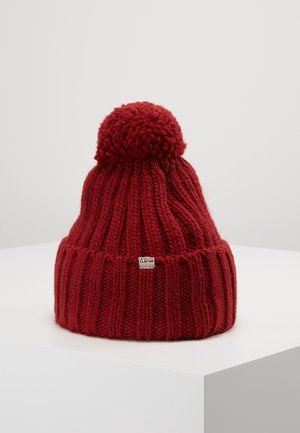 Bonnet rouge en tricot avec un grand pompon sur le dessus et un revers plié doté d'une petite étiquette métallique de la marque.