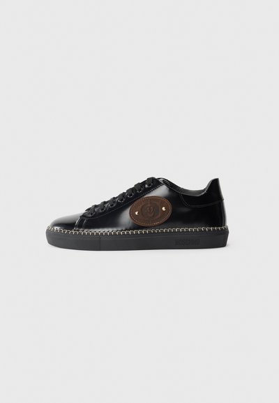 Baskets en cuir verni noir avec un bout rond, patch en cuir marron avec logo, lacets noirs et couture contrastante le long de la semelle.