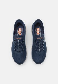 Marinblå mesh-sneakers med elastiska snören, vadderad krage och kontrasterande grå detaljer. Lätt sula med slip-on design för enkel påtagning.