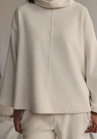 Sweatshirt oversized in crema con costa a coste, dotato di colletto alto, spalle scese e orlo dritto, realizzato in tessuto morbido e testurizzato.