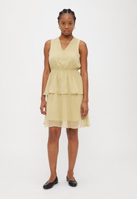 Rochie fără mâneci, de un galben deschis, cu un design stratificat, având un decolteu în V și un tipar cu buline. Fabricată dintr-un material fin și transparent.