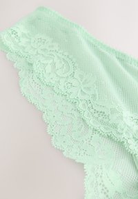 Material din dantelă verde mentă cu modele florale, margini ondulate și un fundal texturat din plasă, evidențiind detalii complexe.