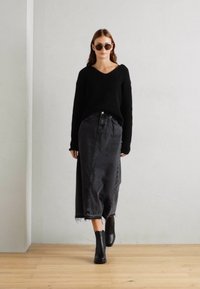 Pull en maille noir avec un col en V, associé à une longue jupe en denim grise et des bottines noires. Texture lisse, design minimal.