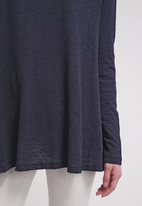 Granatowa bluzka z długim rękawem o luźnym kroju i lekkiej teksturze; charakteryzuje się zaokrąglonym dołem oraz miękkim, lekko melanzowym wyglądem.