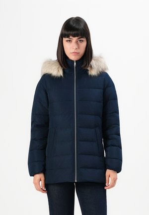 Veste matelassée navy avec une bordure en fausse fourrure sur la capuche, design matelassé vertical, fermeture éclair, et poches latérales pour plus de praticité.