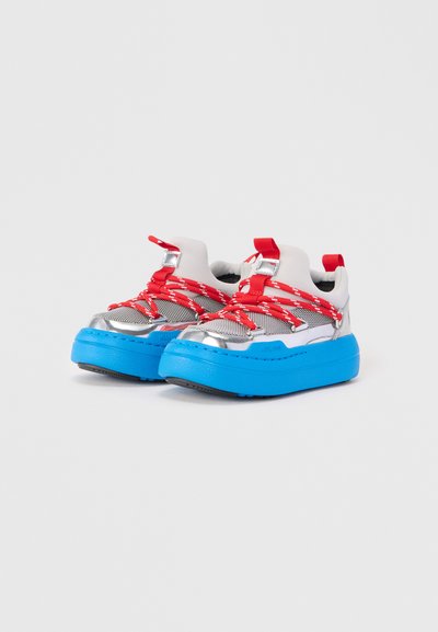 Baskets chunky avec une tige grise, des accents métalliques, des lacets rouges et blancs, et une épaisse semelle bleue. Matériau texturé avec col rembourré.