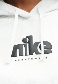 Λευκό φούτερ από φλίς με μεγάλο μαύρο λογότυπο Nike και κείμενο «sportswear» από κάτω. Διαθέτει κουκούλα με κορδόνια και απαλή υφή.