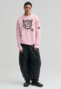 Hosszú ujjú rózsaszín ing fekete grafikai mintával és oversized fekete nadrággal. Jellemzője a laza szabás és a texturált anyag.