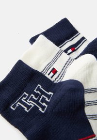 Tres pares de calcetines de algodón: azul marino, blanco con rayas y estampados. Presentan un logo, colores contrastantes y puños acanalados.