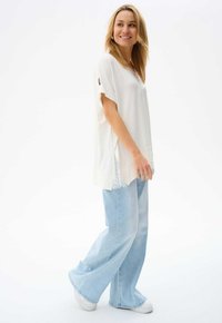 Witte top met korte mouwen en kantdetail, gecombineerd met lichtblauwe wijde jeans en witte sneakers, wat een casual, ontspannen outfit creëert.