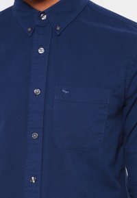 Marineblauwe button-down overhemd van glad katoen, met een borstzak met geborduurd logo en zilveren knopen langs de knoopsluiting.