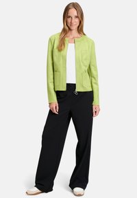 Zielona kurtka z imitacji zamszu z zamkiem błyskawicznym, dwoma przednimi kieszeniami, okrągłym dekoltem, połączona z czarnymi spodniami o szerokich nogawkach i białymi sneakersami.