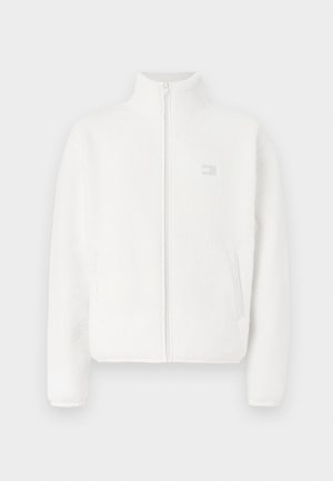 White fleece jacket with high collar, front zipper, and side pockets. Features a small logo in gray on the upper left side. Soft texture.