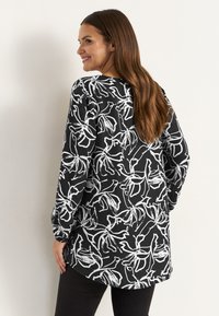Svart blus med vitt blommönster, lös passform, långa ärmar, rundad fåll, tillverkad av lättviktigt tyg, har en slät yta.