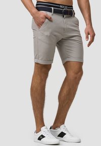 Graue Shorts mit aufgerollten Säumen, zwei vorderen Taschen und einem strukturierten Marineblauen Gürtel. Getragen mit weißen Sneakers mit schwarzen Akzenten.