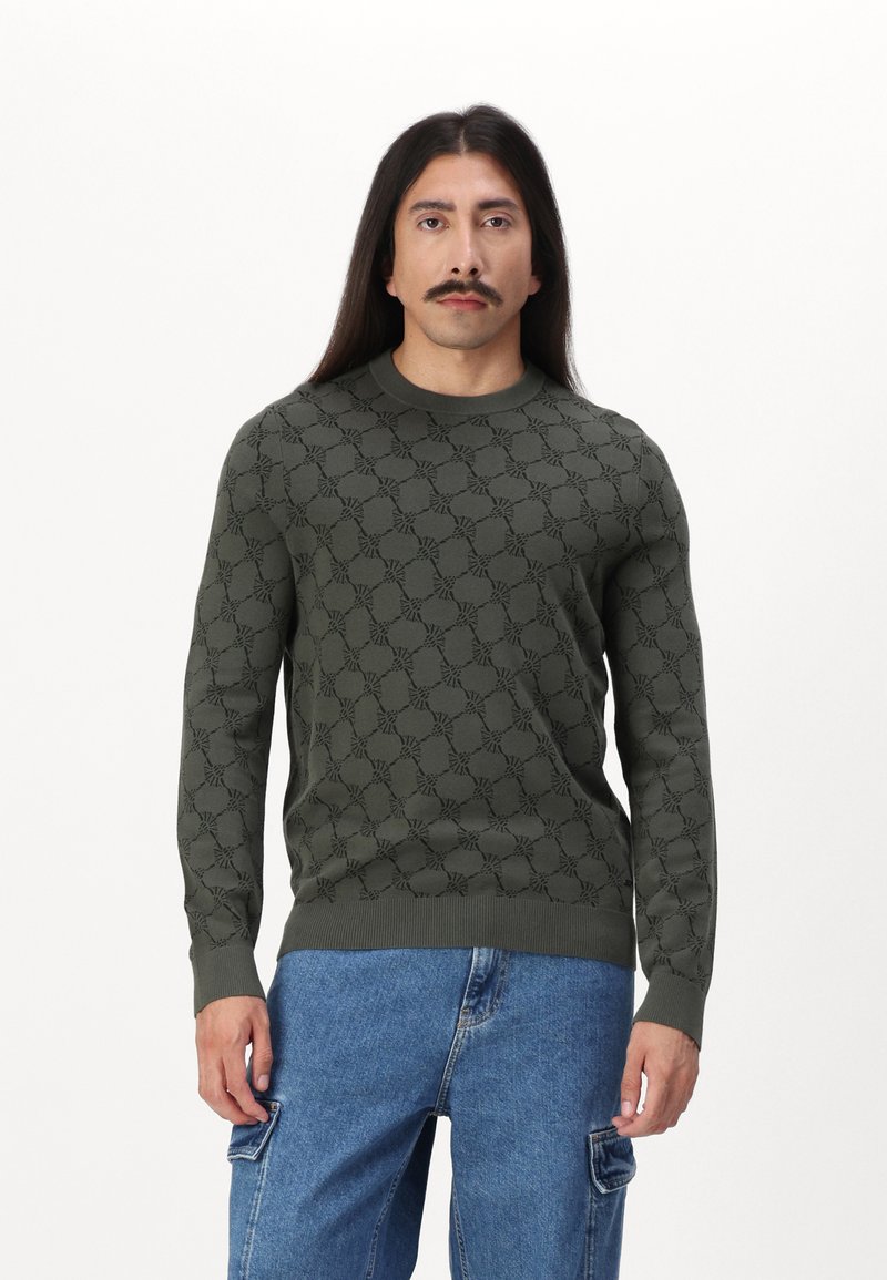 Olivgrüner gestrickter Pullover mit einem strukturierten Blumenmuster, rundem Halsauschnitt und gerippten Bündchen, kombiniert mit hellblauen Cargo-Hosen.