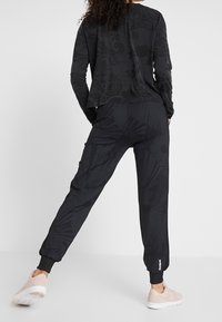 Black athletic outfit featuring a long-sleeve top and tapered pants, with a subtle floral pattern, elastic cuffs, and a logo accent on pants.