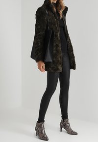 Konstpälsjacka i olivgrönt med hög krage, kombinerad med svarta leggings och spetsiga ankelboots med ormmönster. Svart tygväska.