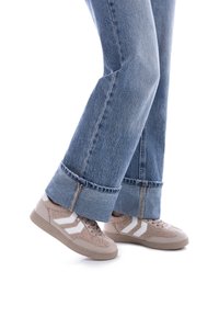 Zapatillas beige con rayas blancas, de ante y tejido texturizado, combinadas con unos vaqueros de mezclilla azul de pierna acampanada con dobladillo deshilachado.