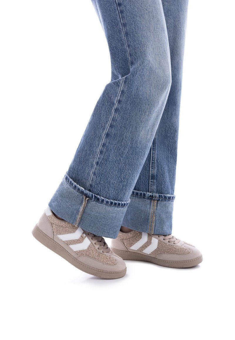 Zapatillas beige con rayas blancas, de ante y tejido texturizado, combinadas con unos vaqueros de mezclilla azul de pierna acampanada con dobladillo deshilachado.
