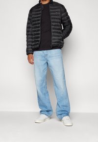 Musta toppatakki vetoketjulla edessä, resorilla varustetut hihansuut, mustan t-paidan päällä, yhdistetty vaaleansinisiin leveälahkeisiin farkkuihin ja valkoisiin lenkkareihin.