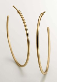Los pendientes de aro en tono dorado cuentan con un diseño suave y redondeado, con un perfil delgado y cierre abierto en la parte superior. La superficie es brillante y reflectante.