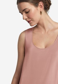 Ärmlös, rosa topp med en slät, blank yta och rundad halsringning, med en avslappnad passform och minimala sömmar.