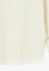 Kremowa, długosleeve koszula wykonana z miękkiego materiału, charakteryzująca się gładką fakturą i przeszytym dołem. Na boku przyszyta jest mała metka z logo marki.