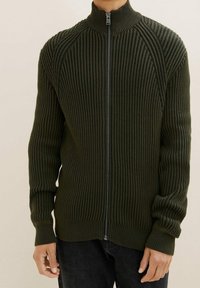 Mörkgrön ribbade zip-up tröja med hög krage, figursydd design och långa ärmar. Slät struktur med ett strukturerat mönster genomgående.