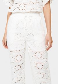 Witte geborduurde broek met oogjes uitsparingen, een losse pasvorm en een trekkoord in de taille, met bloem- en cirkelpatronen erdoorheen.