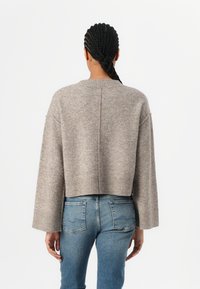 Lyhennetty, beige neulepaita pitkät hihat ja joustava helma. Pehmeässä tekstuurissa on hienovarainen sävy ja leveä pyöreä kaula-aukko.