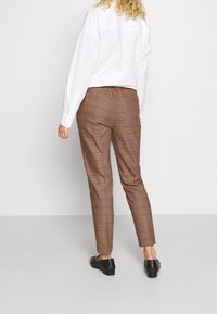Bruine geruite broek met een getailleerde pasvorm, voorzien van een platte voorkant, achterzakken en een licht taps toelopende pijp, gecombineerd met een witte overhemd met kraag.
