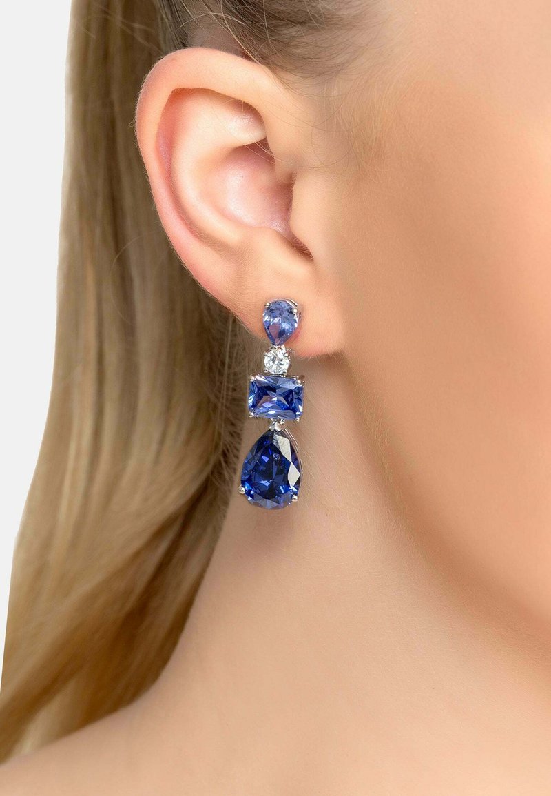 Orecchini a goccia di cristallo blu con gemma a forma di pera, accentuazione rettangolare e parte superiore rotonda. Montati in metallo argentato con accenti scintillanti.