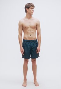 Ανδρικά μαγιό σορτς σε σκούρο τιρκουάζ, ελαφρύ υλικό με ελαστική μέση, κορδόνι σύσφιξης και διακοσμητικά σχέδια στο πλάι.