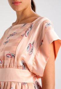 Vestido de satén rosa con mangas cortas, que presenta un patrón de pequeños paraguas. Textura suave con un corte holgado y cintura elástica.